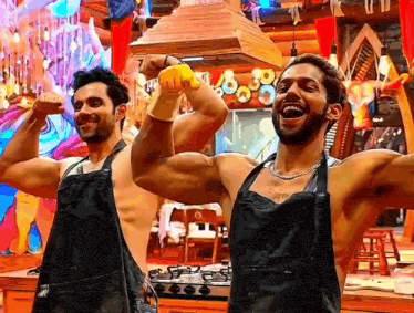 a couple of men wearing aprons are flexing their muscles in a kitchen .