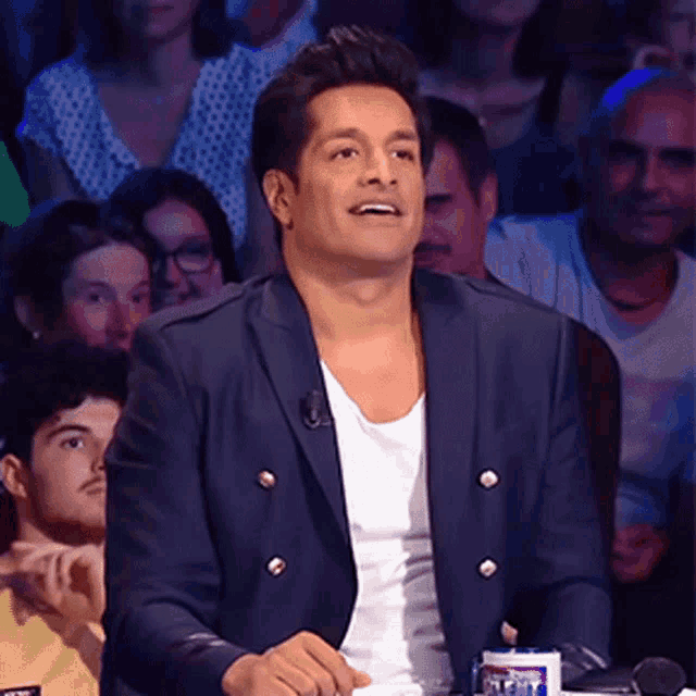 a man sitting in front of a crowd wearing a blue jacket and a white shirt