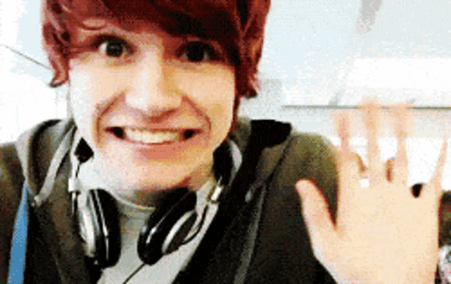 a young man wearing headphones smiles and waves his hand