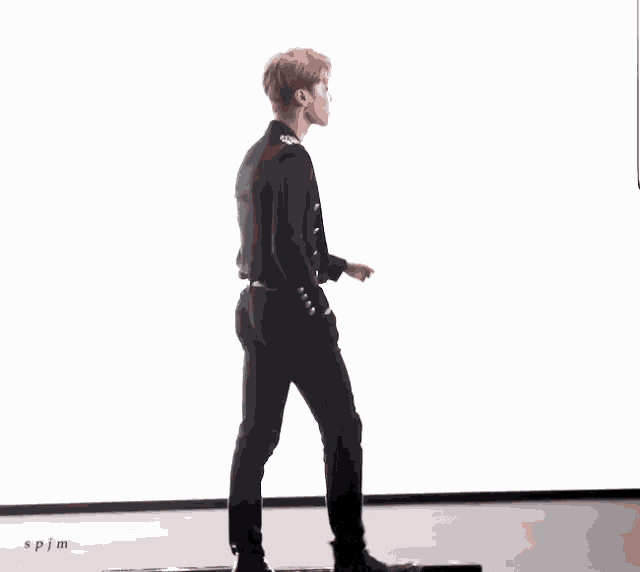 a man in a black suit is walking across a white wall