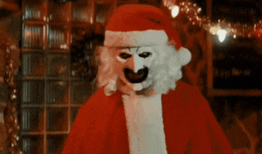 a clown dressed as santa claus is standing in front of a brick wall .