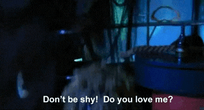 a man with dreadlocks and red lipstick is wearing a blue shirt and tie and says `` do you love me ? ''