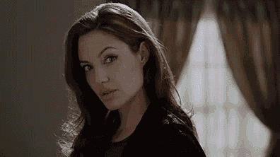 a woman with long brown hair is standing in front of a window in a room .
