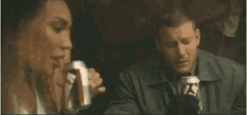 a man is drinking from a can while a woman sits under a tent