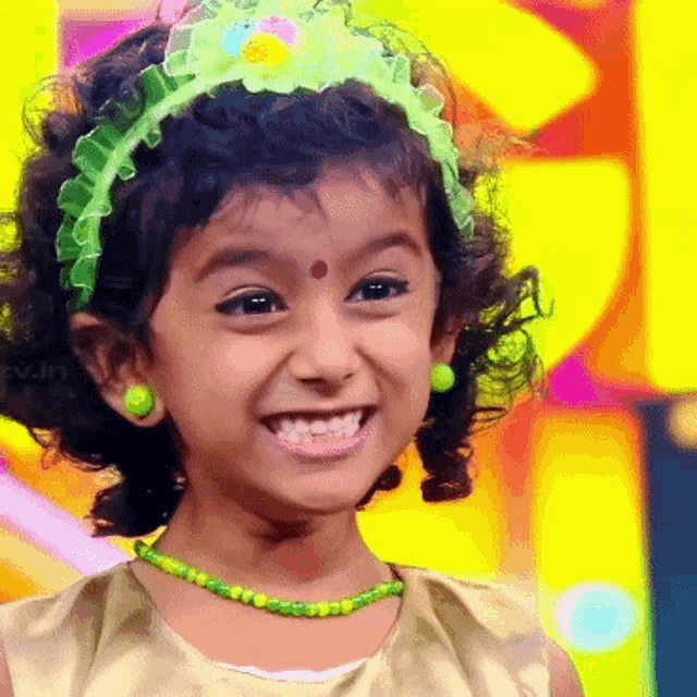 a little girl wearing a green headband and green beads smiles for the camera