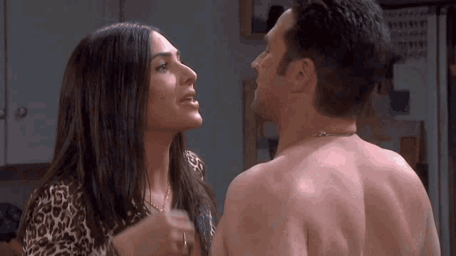a shirtless man and a shirtless woman are looking at each other in a kitchen