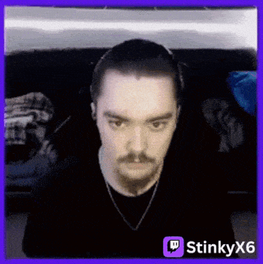 a man with a beard and mustache is sitting on a couch in front of a purple background with a twitch icon