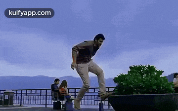 a man is doing a trick on a skateboard while a woman sits on a bench .