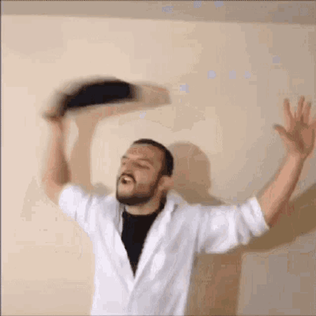 a man with a beard is throwing a hat in the air while wearing a white shirt .