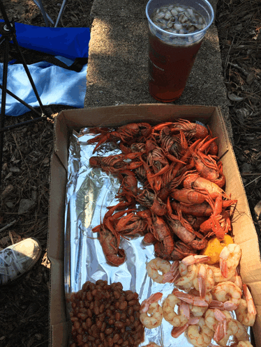 a cardboard box filled with shrimp and beans next to a cup of beer
