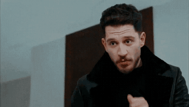 a man with a beard is wearing a black jacket and giving a thumbs up