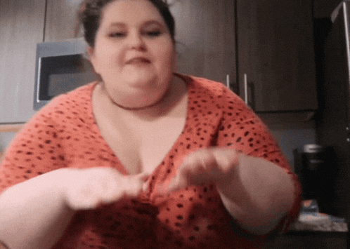 a woman in a red and black polka dot shirt is standing in a kitchen