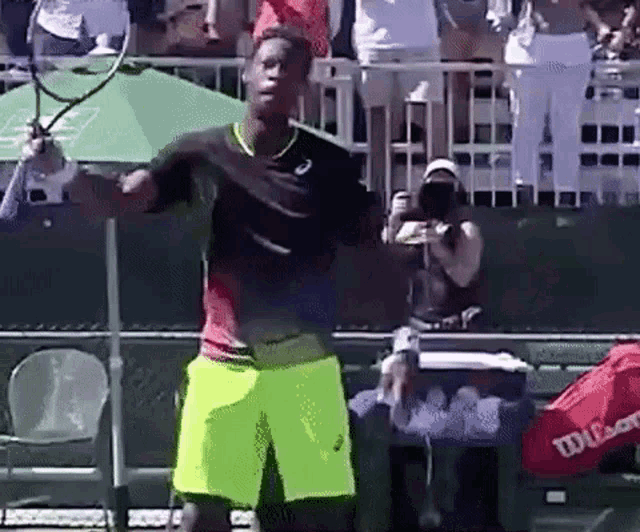 a man holding a tennis racquet on a tennis court with a wilson bag in the background .