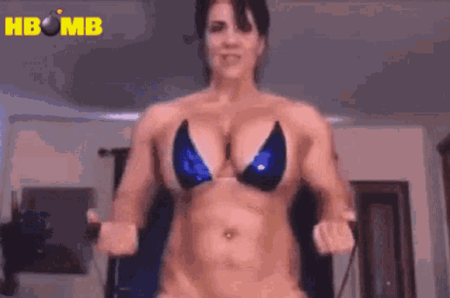 a woman in a bikini is flexing her muscles in front of a sign that says hbomb .