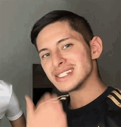 a young man in a black shirt is smiling and waving his hand .