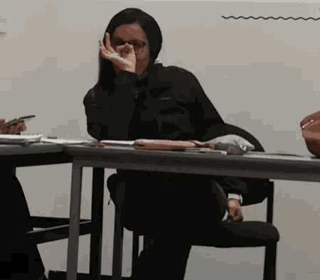 a woman sits at a desk with her hand over her mouth