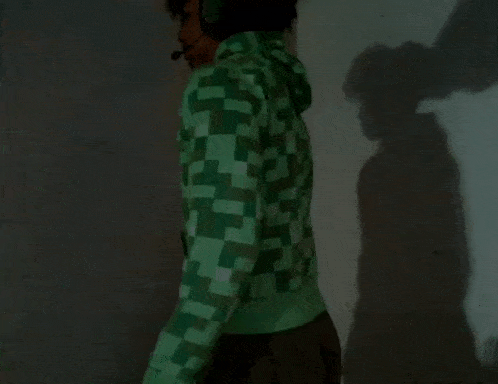a man wearing a green jacket and headphones stands in front of a wall