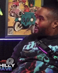 a man wearing a shirt that says hilly wave is sitting in front of a microphone