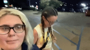 two women are posing for a picture in a parking lot at night .