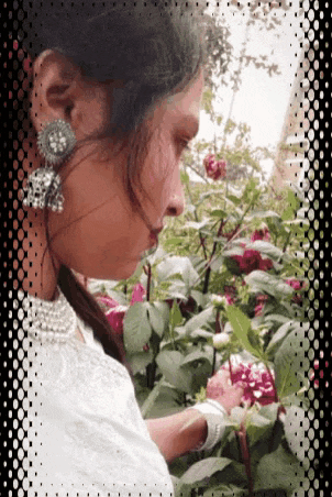 a woman in a white dress is standing in front of a bush of flowers