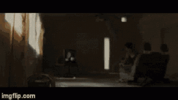 a man is sitting on a couch in a dark room with smoke coming out of a window .