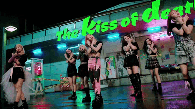 a group of girls are dancing in front of a sign that says " the kiss of death "