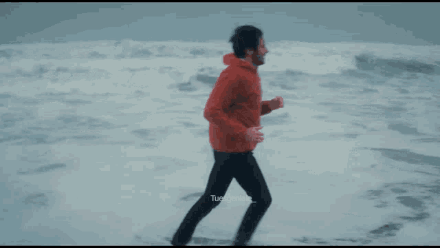 a man in a red jacket is standing in the ocean with the caption tuesgenial_