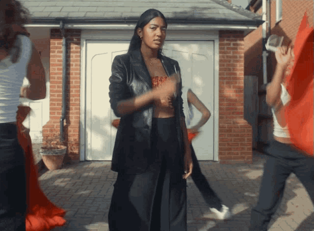 a woman in a black jacket is dancing in front of a garage