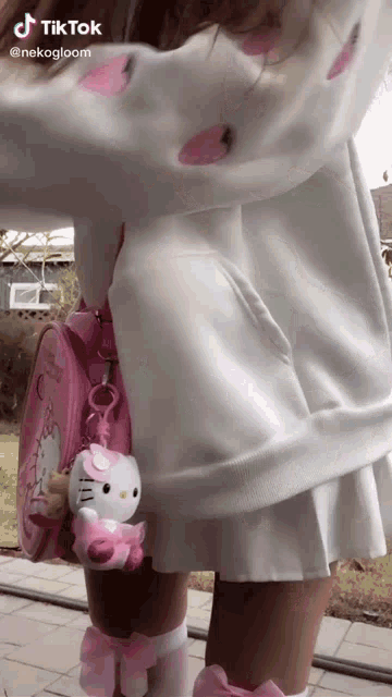 a girl is wearing a white dress and a pink hello kitty purse .