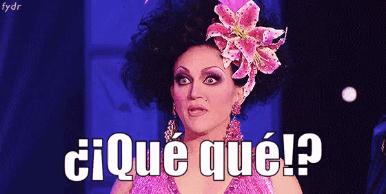 a drag queen is wearing a pink dress and a flower in her hair and says ¿ que qué ?