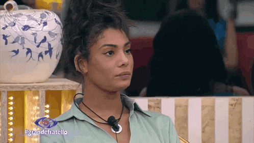 a woman in a green shirt is sitting in front of a vase with the words grandefratello on the bottom