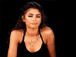 a woman in a black tank top and a necklace is making a funny face .