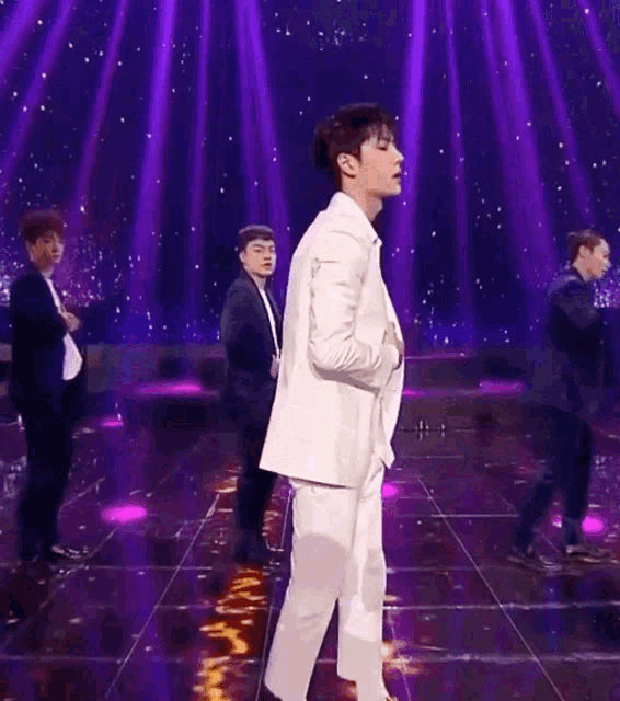 a man in a white suit is standing on a stage with a man in a black suit behind him .