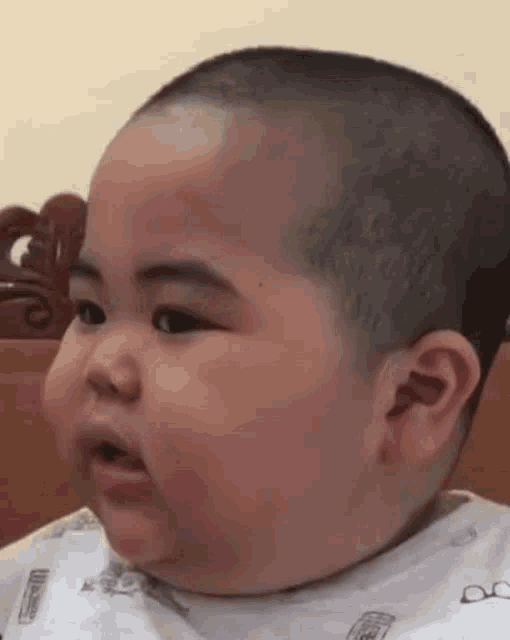 a baby with a bald head is sitting on a bed making a funny face .