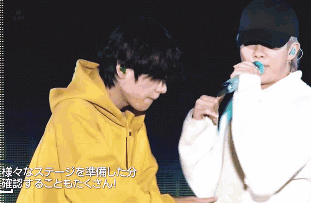 a man in a yellow hoodie stands next to a man in a white sweater