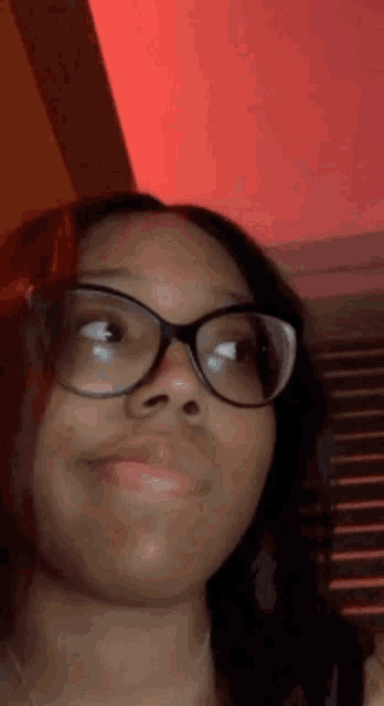a woman wearing glasses is making a funny face in front of a red light .