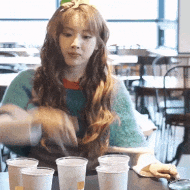 a woman in a green sweater is sitting at a table with a bunch of cups
