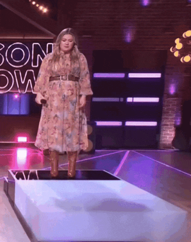 a woman in a floral dress is standing on a stage in front of a sign that says son down