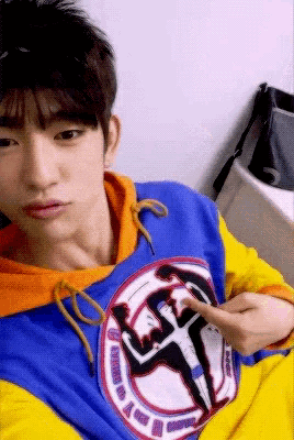 a young man wearing a blue and yellow sweatshirt with a picture of a man on it pointing at it