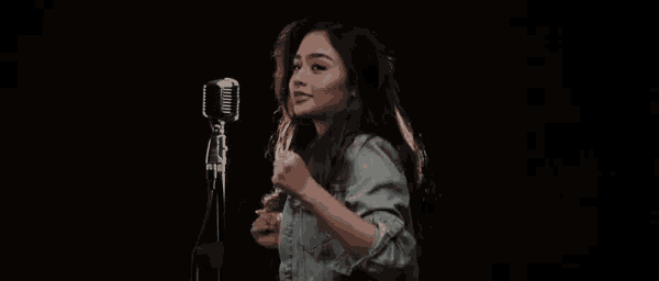 a woman is standing in front of a microphone in a dark room with her arms outstretched .