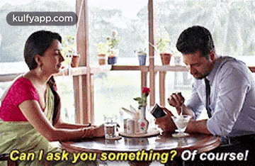 a man and a woman are sitting at a table talking to each other and the man is looking at his phone .