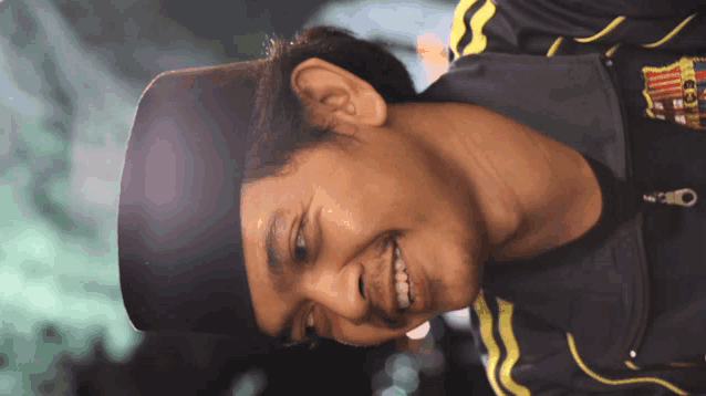 a man wearing a black hat and a black jacket with a yellow stripe on the sleeves is smiling