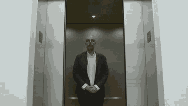 a man in a suit stands in an elevator with a sign on the wall that says ' exit '