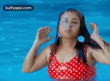 a woman in a red polka dot bikini is swimming in a pool and blowing bubbles .