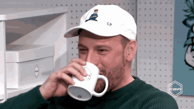 a man wearing a hat that says cp on it drinks from a mug