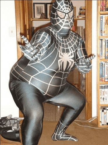 a man in a spiderman costume is squatting down in front of a bookshelf