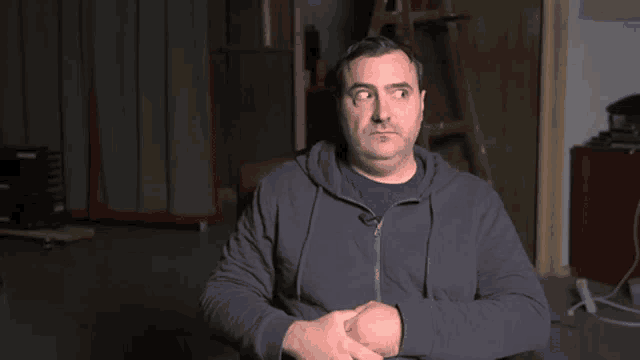a man in a hoodie is sitting in front of a ladder