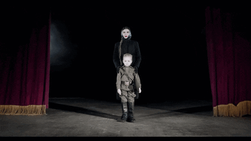 a man and a child are standing on a stage with a red curtain behind them