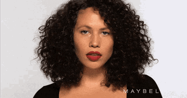 a woman with curly hair is wearing red lipstick and a black shirt with the word maybelline on it