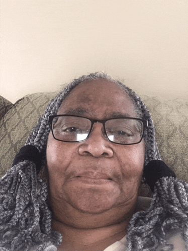 an elderly woman wearing glasses and braids is smiling